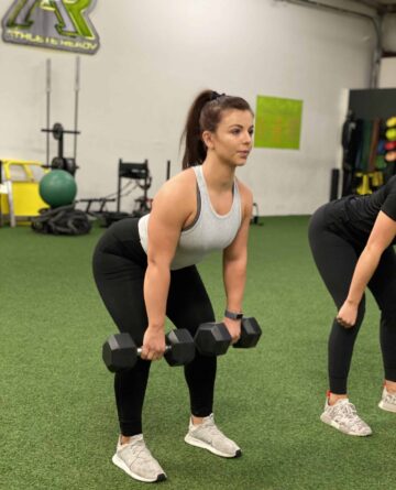 A female athlete doing a deadlift with dumbbells.