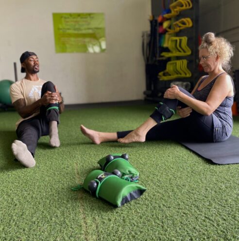 WELLNESSSS A client and a coach sitting on the ground working on ankle mobility drills.
