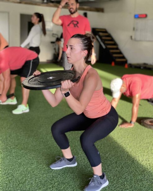 adult-class A woman doing squats with a weighted plate.