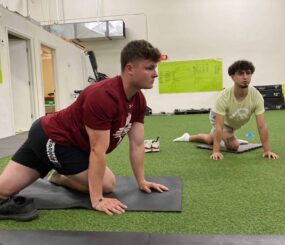 Two male athletes doing GOATA Corner Hip Stretch excercises.