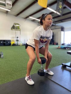 A female youth athlete doing a goblet squat with a dumbell.