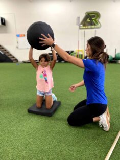 A coach helping a youth athlete do medicine ball trows from the knees.