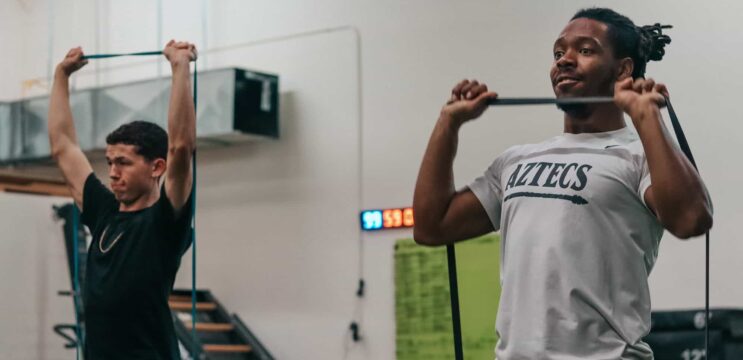 Two male athletes doing overhead banded pull-aparts.